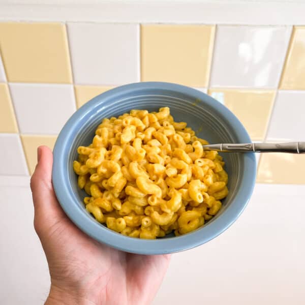 Bowl of creamy vegan mac and cheese held in front of a kitchen backsplash